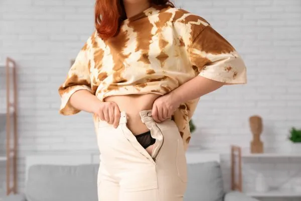 Image of woman trying to do her trousers up after pregnancy weight gain Owsestry