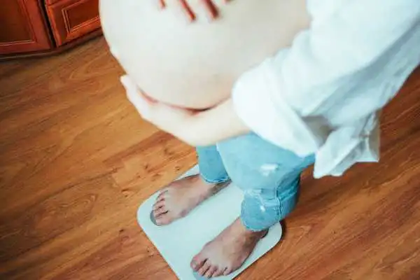 Image of woman weighing herself and experiencing weight gain through pregnancy Owsestry
